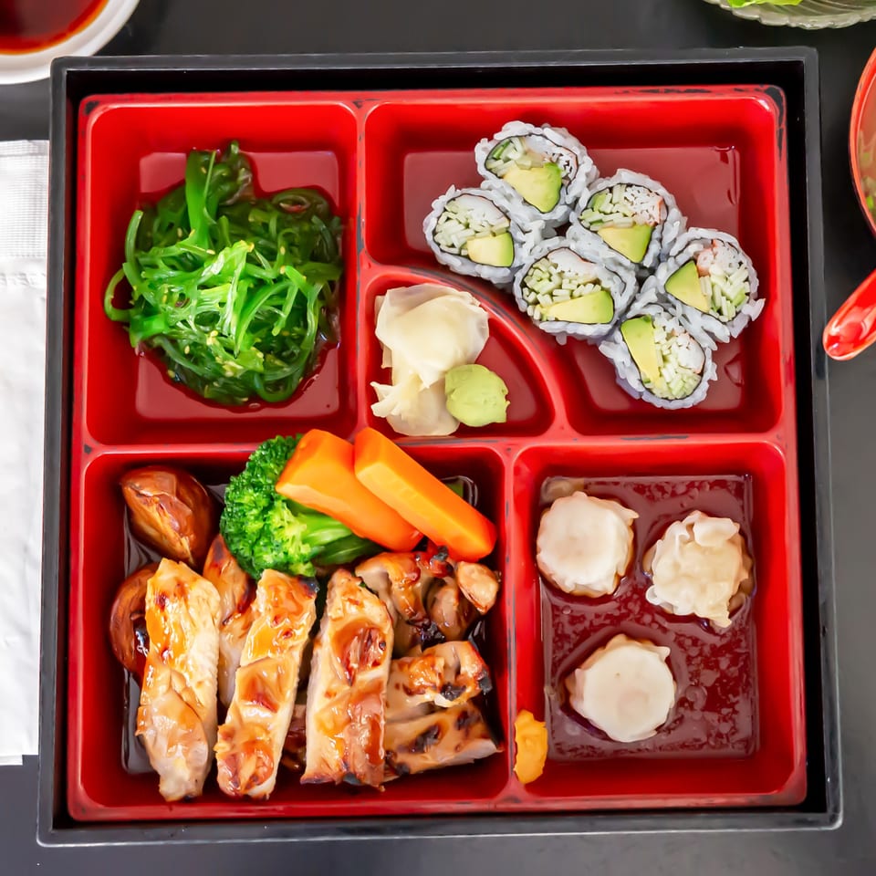 Koiso Japanese Restaurant's bento box with seaweed salad, sushi, teriyaki chicken, vegetables, and dumplings.