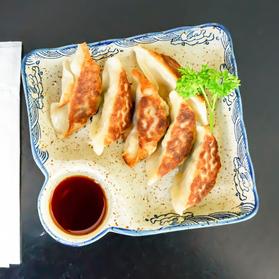 Pan-fried gyoza dumplings with crispy bottoms, garnished with parsley and served with soy sauce.