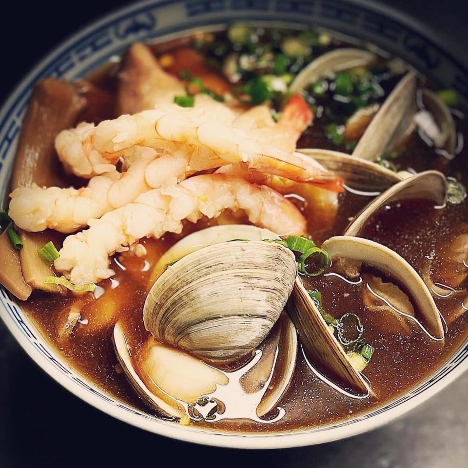 A bowl of Koiso Japanese Restaurant's seafood soup with shrimp, clams, and green onions.