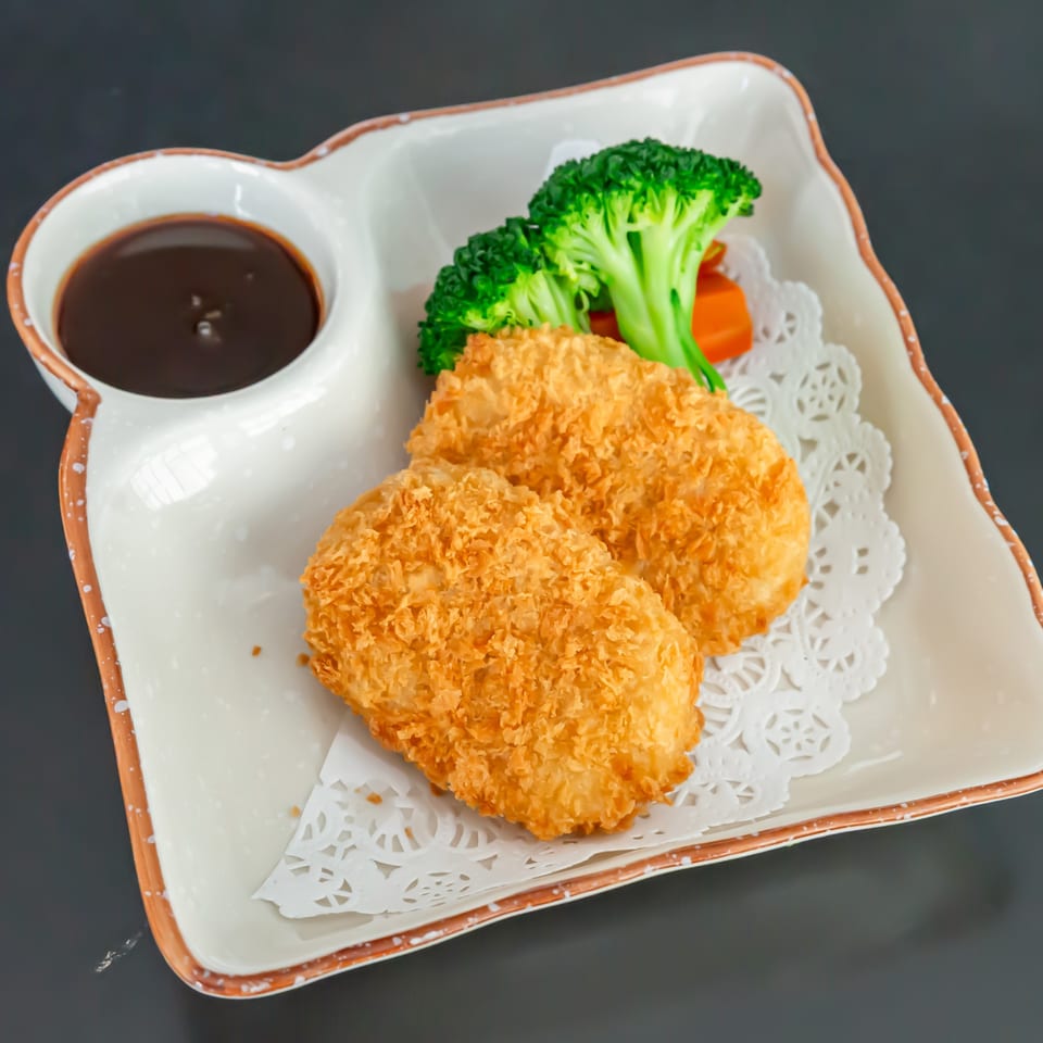 Two golden-brown fried cutlets with broccoli, carrots, and a side of dark sauce on a white plate.